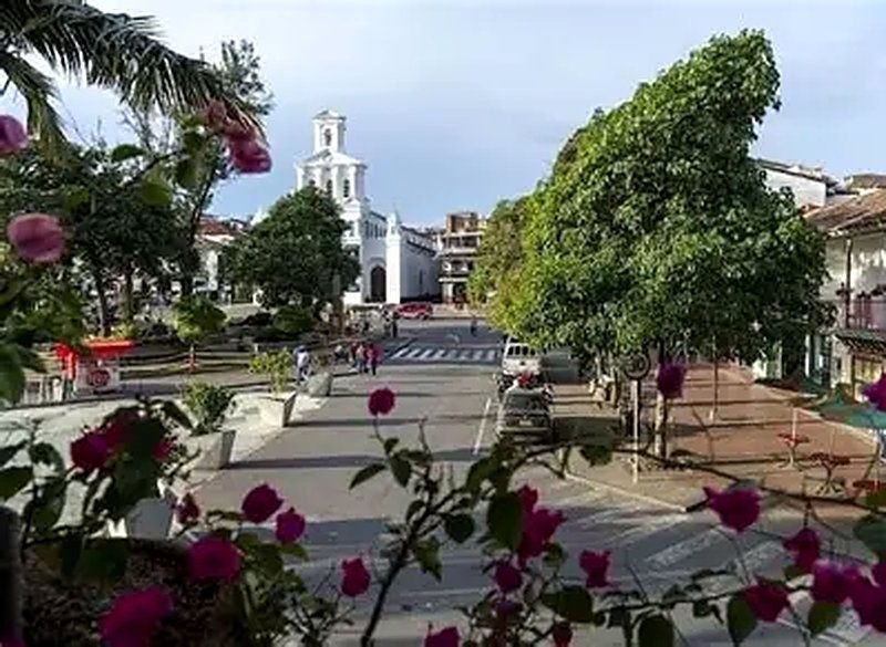 Calle del centro histórico de Marinilla con su iglesia blanca al fondo y flores en primer plano