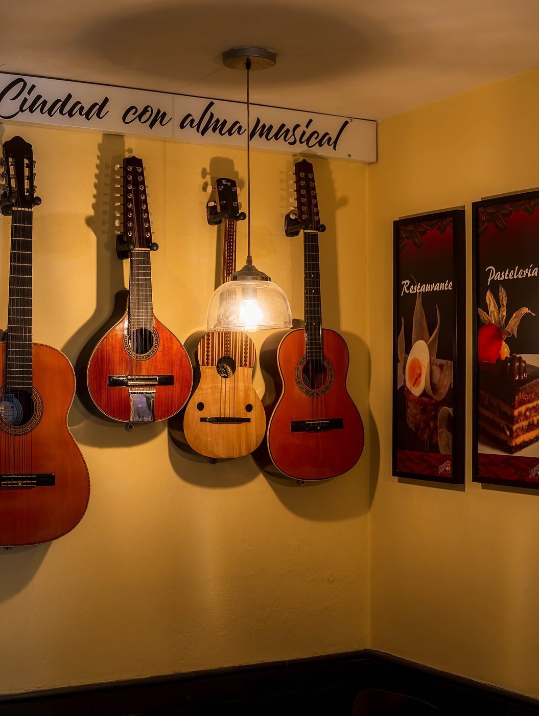 Pared de Ritus Café con guitarras, tiples y bandolas bajo el letrero Ciudad con alma musical